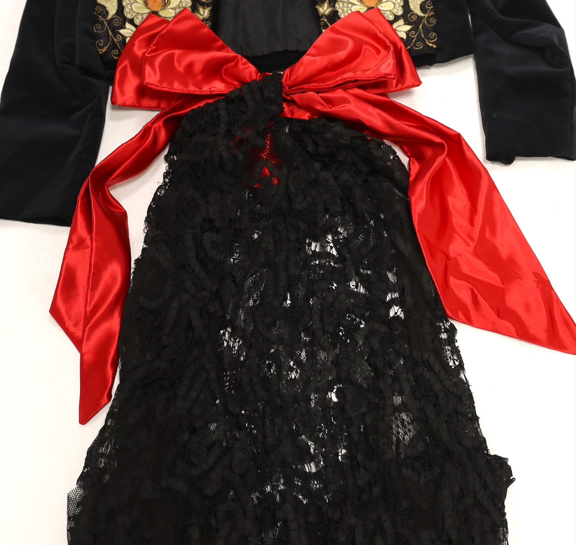 A velvet bolero with ornate polychrome silk embroidered and beaded panels, together with a full length black tape lace evening skirt (some damage) with red satin waisted sash